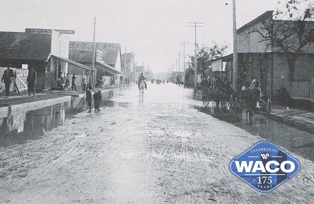 Black and white photo. People walking in flooded road.