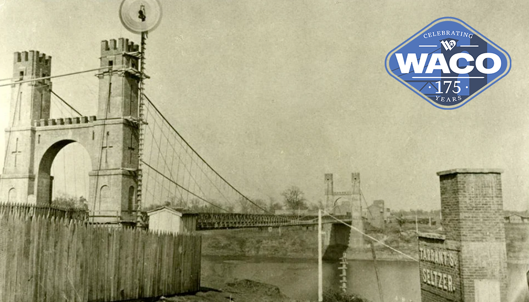 Black and white photo of the Waco Suspension Bridge with a fence around the toll keepers cottage