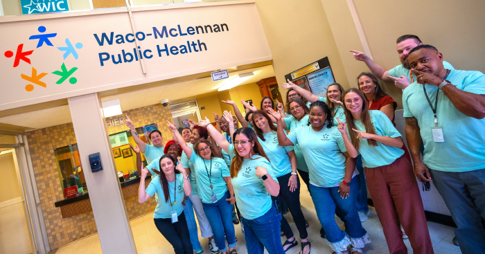 Group of people pointing to the new Waco-McLennan Public Health logo