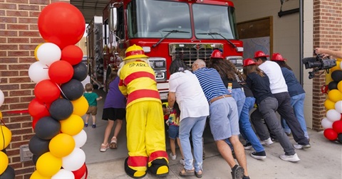 Group of people and Sparky the Fire Dog pushing a fire engine into the station